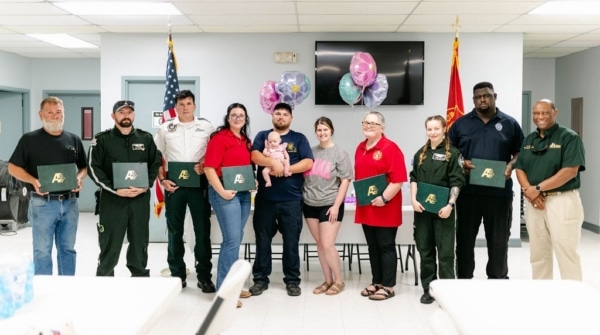 A group of first responders take a group picture with the family of the infant they helped save.